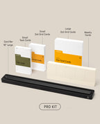 A neatly arranged set of stationery items labeled as the “Analog Card Bar - Pro Kit (Black),” featuring task cards, dot grid cards in two sizes, weekly cards, and a long black Analog Card Bar displayed on a beige background.