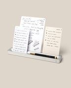 The Analog Card Bar (Small 10" - Silver) neatly holds a pen and three notepads with handwritten notes, sketches, and to-do lists, all set against a plain beige background.