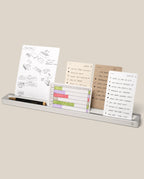 The Analog Card Bar (Large 16" – Silver) is a slim solid aluminum desk organizer that holds a pen and several task cards with handwritten notes, sketches, and lists, all neatly arranged against a beige background.