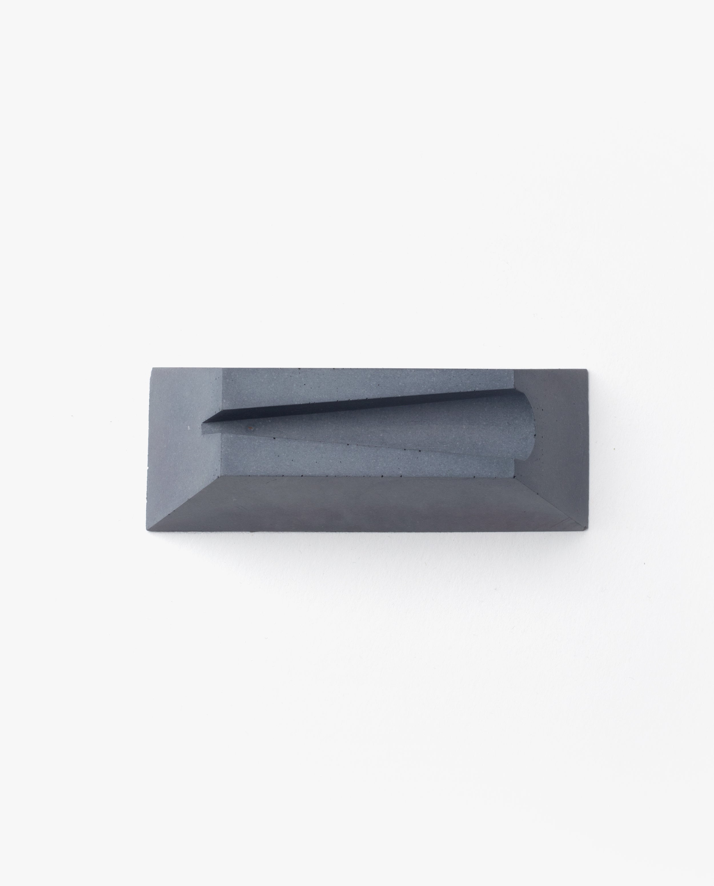 A rectangular, dark gray cast concrete Craighill Desk Knife Plinth (Slate) with a sloped, angular groove on top is shown as a sleek holder, set against a plain white background.