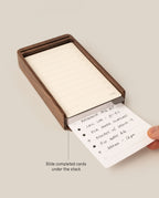 A hand slides a task card under a stack in the Analog Daily Focus Kit (Walnut)—a sleek wood card holder for your daily tasks, such as research, calls, podcasts, repairs, and appointments.