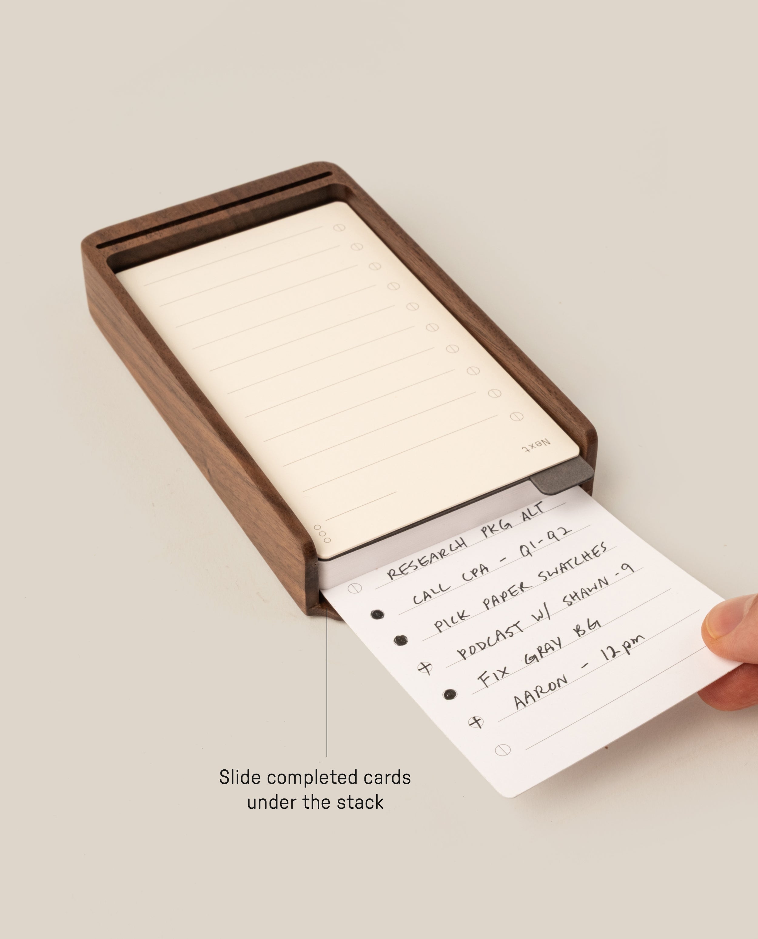 A hand slides a task card under a stack in the Analog Daily Focus Kit (Walnut)—a sleek wood card holder for your daily tasks, such as research, calls, podcasts, repairs, and appointments.