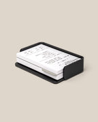 A stack of white Small Dot Grid Cards with handwritten notes is neatly placed in the black aluminum Analog Capture Kit - Small, set against a plain beige background.