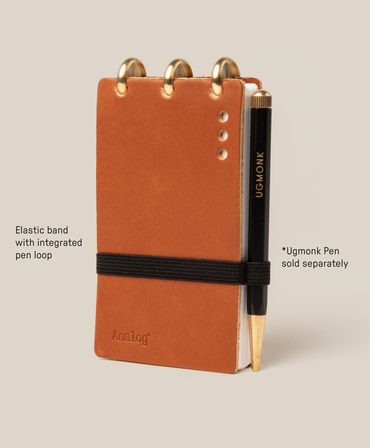 Tan Leather Discbound Analog notebook with three metal rings, featuring full-grain leather covers, an elastic closure band, and a black UGMONK-branded pen in the pen loop. Includes 3 refills. Note: Pen sold separately; compatible with Analog Task Cards.