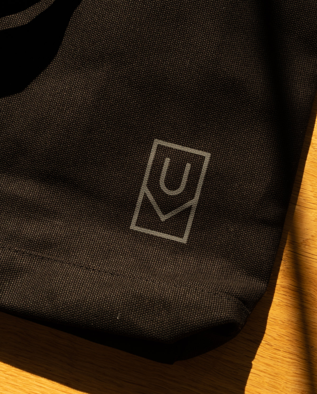 Close-up of a sturdy, black Ugmonk Utility Tote (Black) featuring a gray geometric logo with the letter U inside a rectangle.