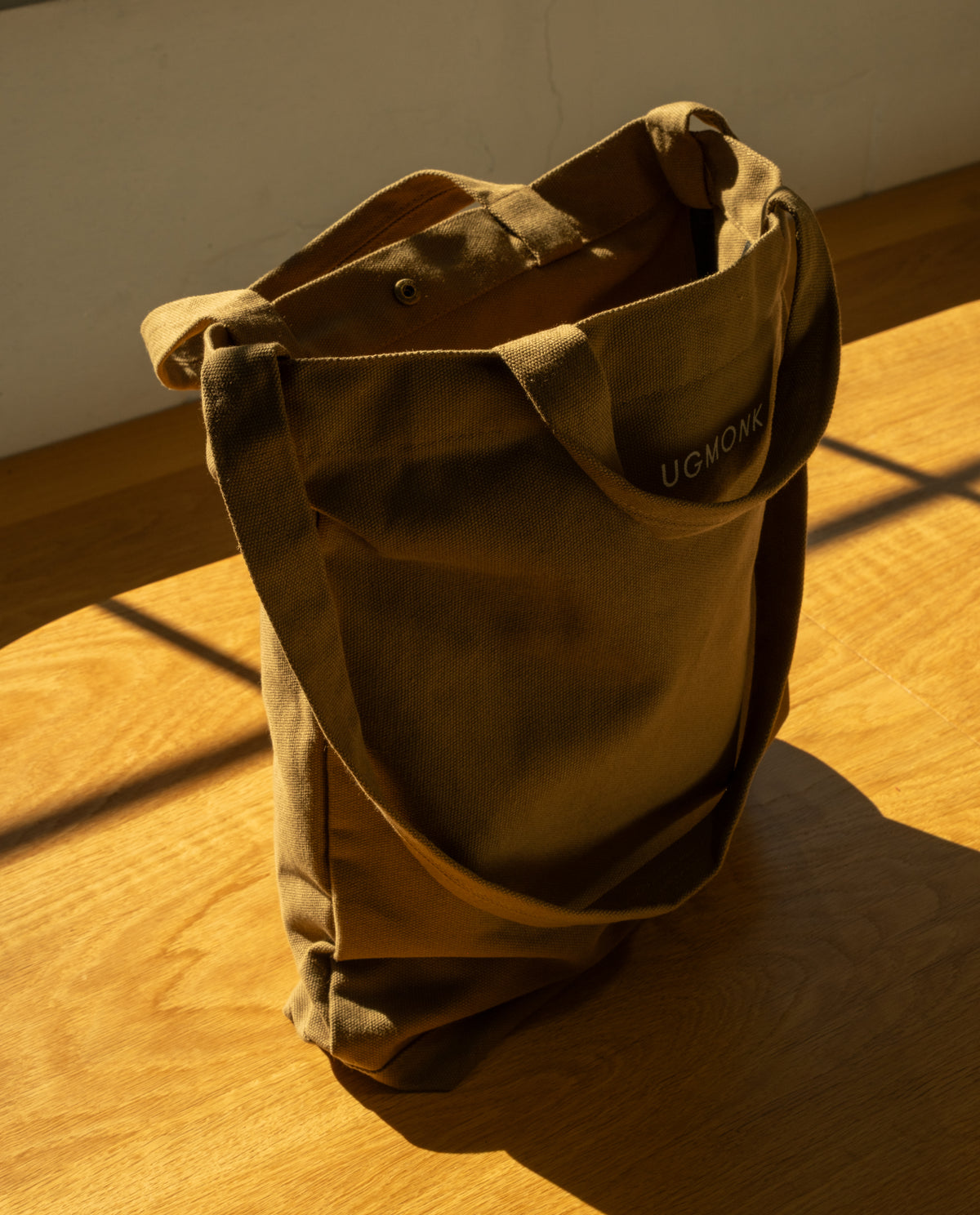 Sturdy olive green Ugmonk Utility Tote (Olive) canvas bag with shoulder straps, shown sitting on a wooden surface.