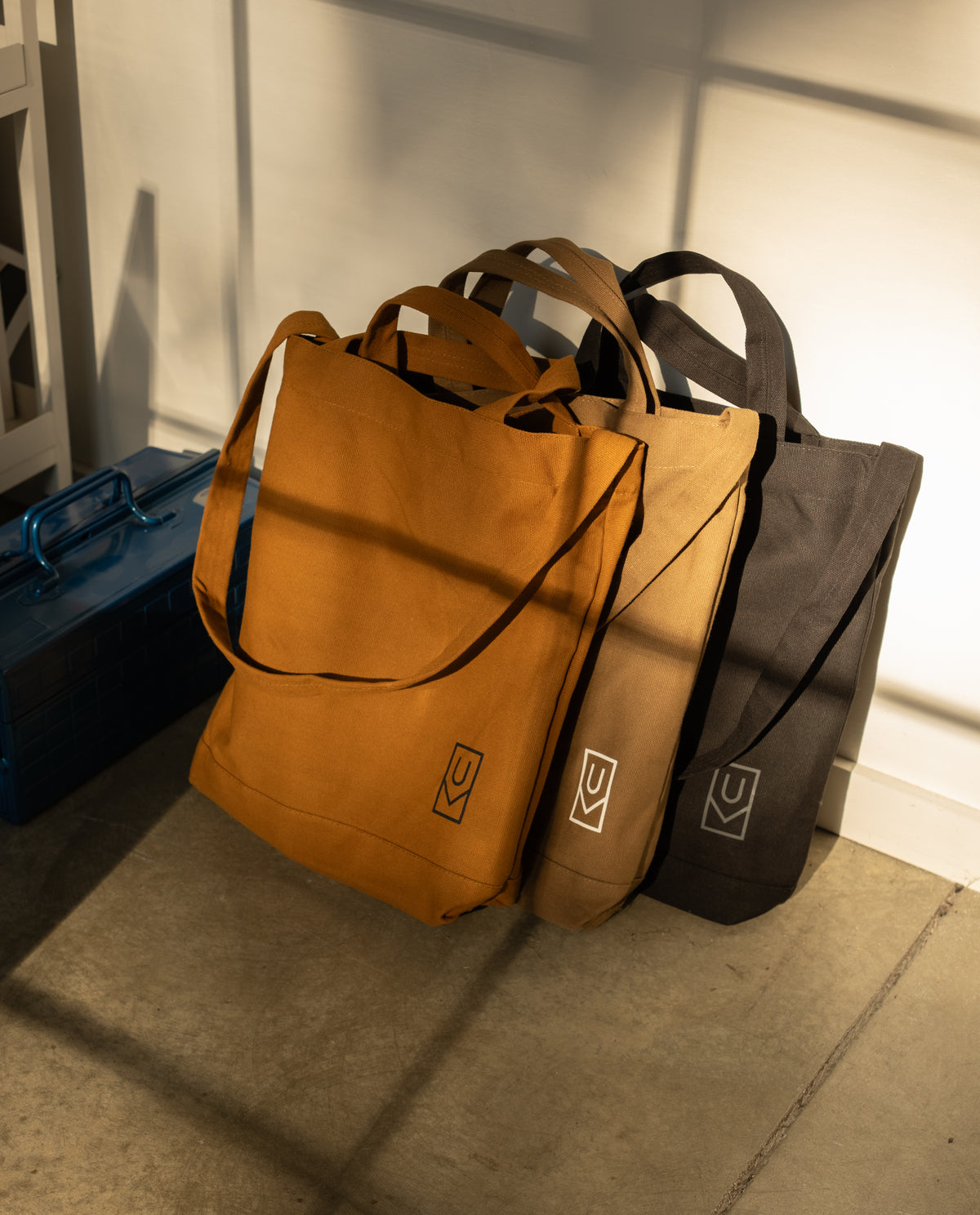 Utility Tote Bundle - Set of 3 featuring three heavyweight cotton totes in rust, tan, and black leaning against a white wall.