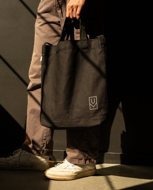 A person holds a durable, heavyweight cotton canvas Utility Tote Bundle - Set of 3 featuring a small geometric logo at the bottom corner.