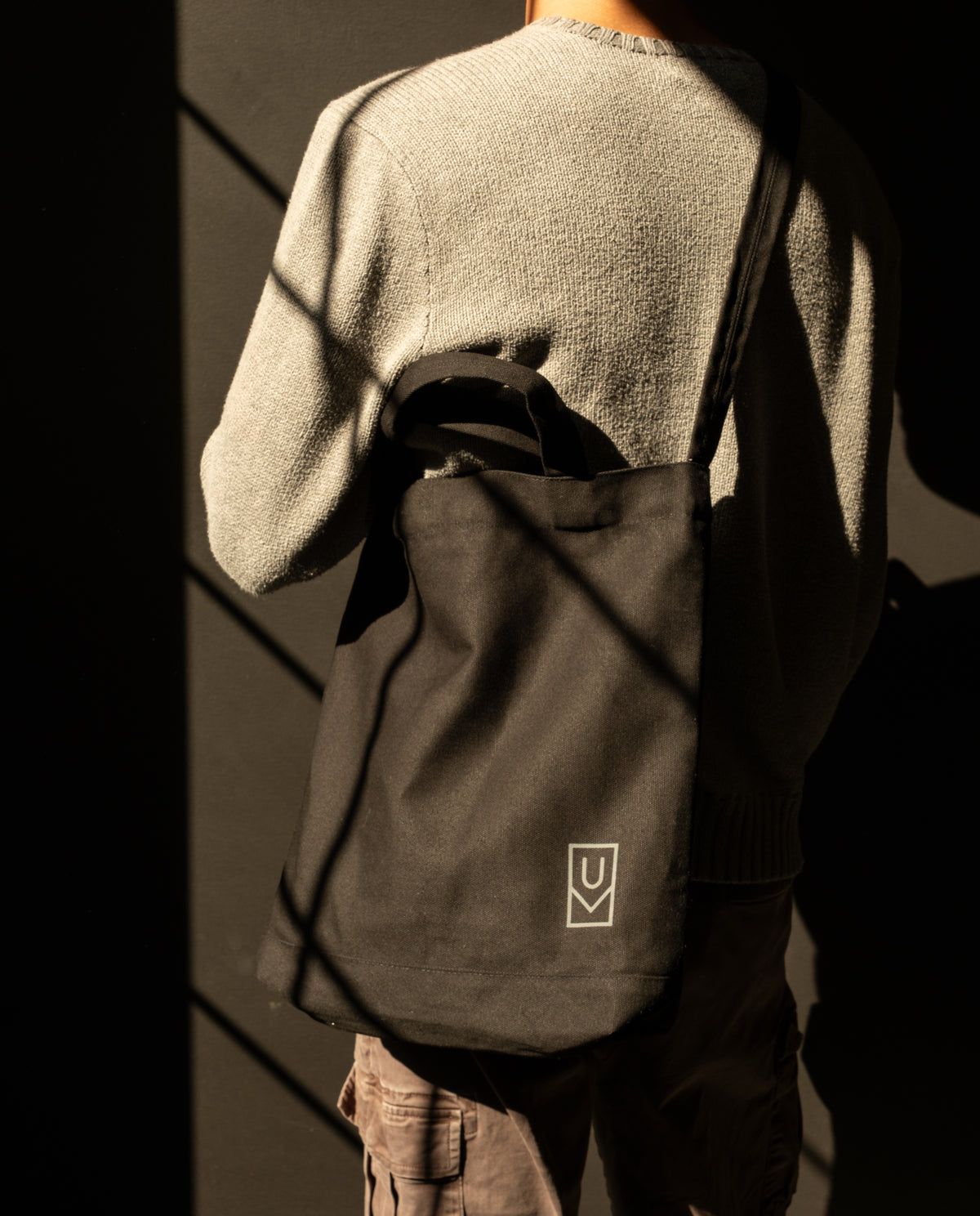 A person wearing a sturdy black Ugmonk Utility Tote (Black) canvas bag over their shoulder with a small rectangular logo on the bottom corner.