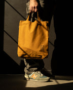 A person holding a sturdy, tan canvas Ugmonk Utility Tote (Field Tan) with a small geometric logo at the bottom.