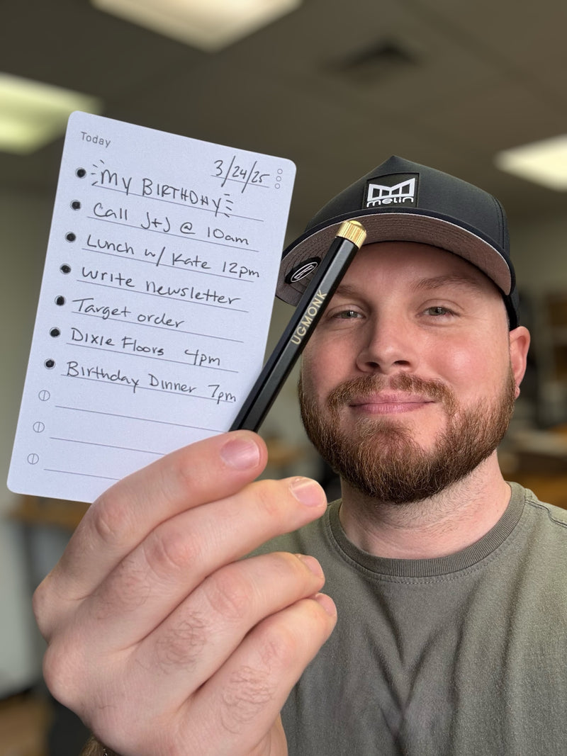A man in a cap smiles, holding a handwritten to-do list for his birthday, including calls, lunch, writing, a target order, a floor task, and a birthday dinner.