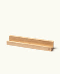 The Analog Weekly Card Holder (Maple) is a simple, rectangular stand made from light maple wood with a groove designed to hold items upright—perfect for displaying your Analog Weekly Cards. Handcrafted in Pennsylvania, this card holder features a small logo engraved on one corner. The background is plain and off-white.