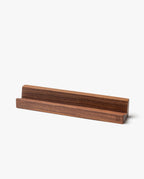 The Analog Weekly Card Holder (Walnut) is a handcrafted, rectangular walnut stand made in Pennsylvania. Its groove holds items like Analog Weekly Cards, phones, or tablets. The visible wood grain and smooth finish add an elegant touch.