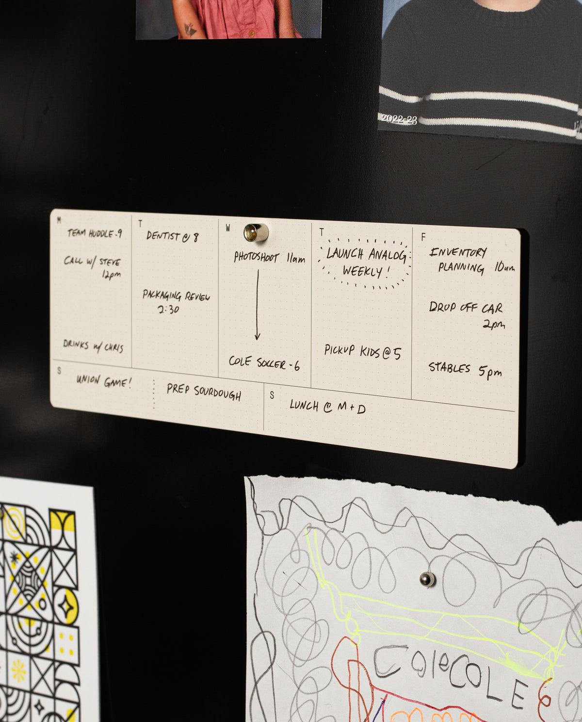 Analog Weekly Cards are pinned to a black wall, displaying handwritten tasks—appointments, calls, inventory planning, and reminders. Below them, colorful drawings and dot grid cards add extra organization and inspiration.
