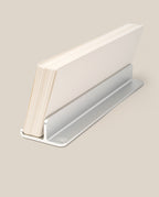 A stack of white Analog Weekly Planning Kit cards is held upright in a sleek silver aluminum stand against a beige background.