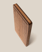 The Analog Travel Case + 3 Card Packs (Walnut), a rectangular case crafted from premium walnut, stands upright on a neutral background, showcasing its smooth surface, grain texture, and chamfered edge. A small engraved logo appears on the top corner of the case.