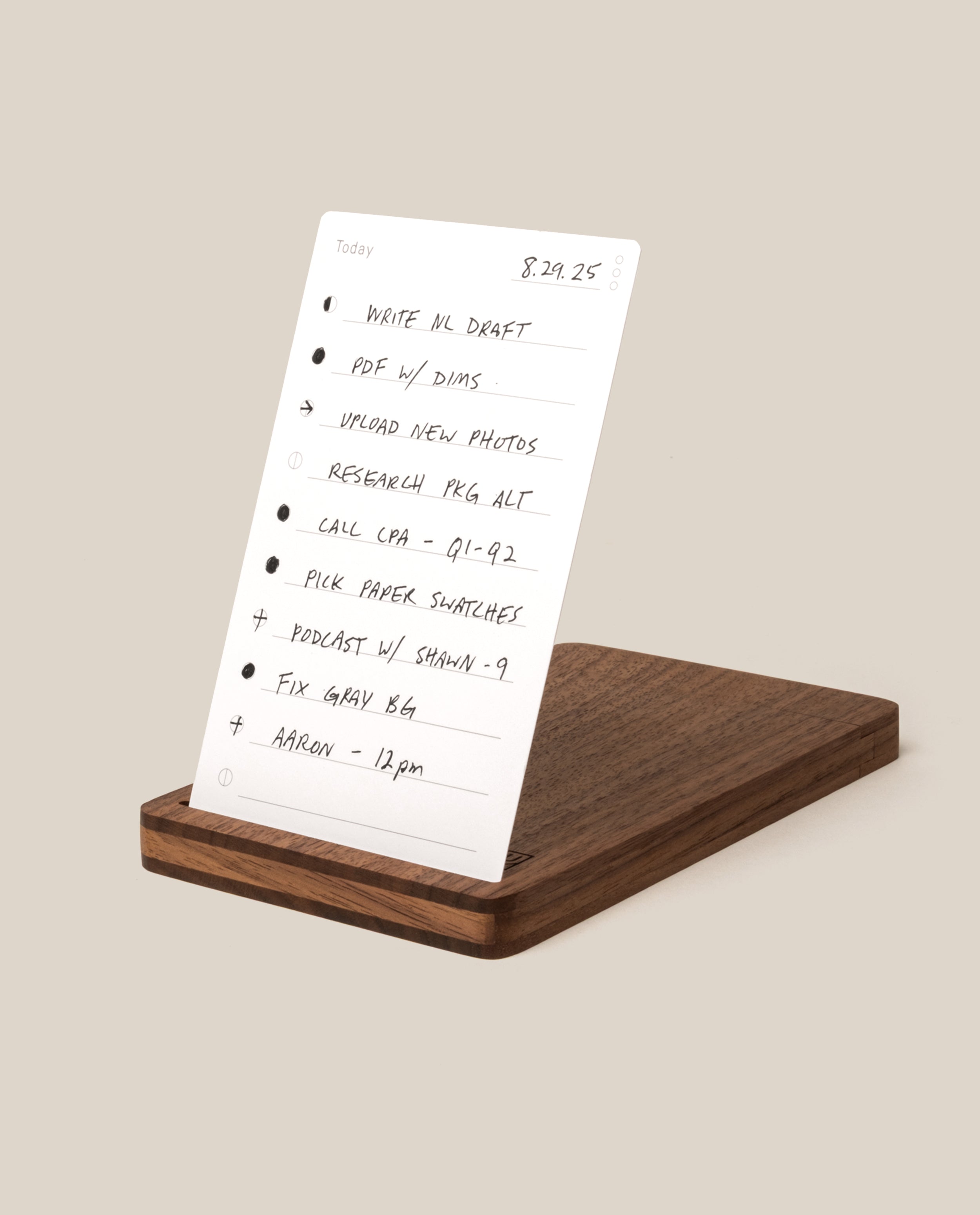 A handwritten to-do list rests on a wooden stand, thoughtfully paired with the Analog Travel Case (Walnut), which features a sleek walnut card holder and magnetic closure. The list includes tasks such as writing a draft, PDF with Dina, uploading photos, research, calls, picking paper swatches, podcasting, fixing gray, and a noon meeting with Aaron.