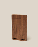 The Analog Bundle (Walnut) is a slim, rectangular walnut card holder with a smooth finish. It stands upright against a plain beige background, featuring a thin horizontal slot near the bottom and a small engraved logo in the corner.