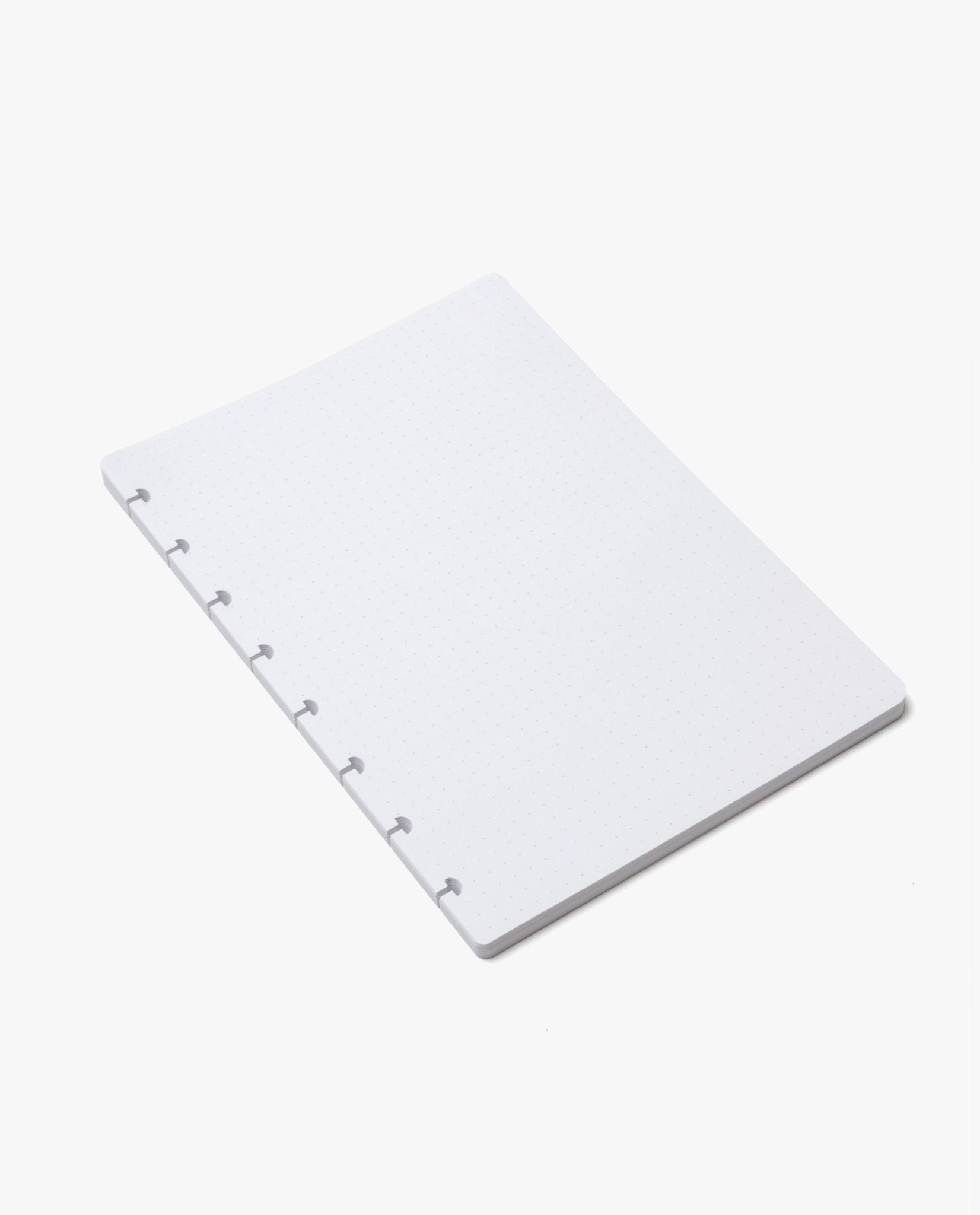 A stack of Discbound Journal Refill (Standard 6" x 8.5") white, loose-leaf dot grid pages with six disc-binding holes along the left edge, designed as a refill paper pack for your Heirloom Discbound Journal, placed on a plain white background.