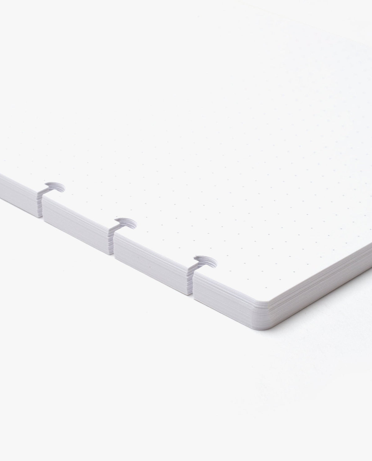 A close-up of the corner of a stack of white, dot grid pages with three mushroom-shaped punched holes, designed as refills for the Discbound Heirloom Journal Bundle (Tan Leather - Standard 6" x 8.5" + 3 Refills), shown against a white background.