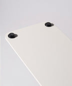 A close-up of the Gather 1x4 Base Plate (White) showcases its white rectangular powder-coated steel surface with two black round rubber feet attached at the corners, set against a plain light gray background.