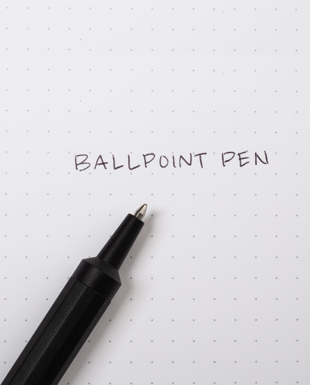 A sleek HMM Ballpoint Pen (Black) rests on dotted white paper with the words BALLPOINT PEN handwritten in black ink. This refillable pen combines elegant design with practicality, making it a standout aluminum ballpoint pen for everyday writing.