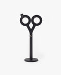 A pair of HMM Scissors (Black) with circular handles stands upright on a magnetic metal base against a plain white background.
