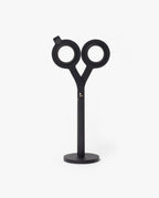 A pair of HMM Scissors (Black) with circular handles stands upright on a magnetic metal base against a plain white background.