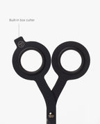 A close-up of HMM Scissors (Black) showcases their round handles, with one handle featuring a labeled built-in box cutter extending from the edge, all set against a white background.
