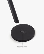 A round, black magnetic metal base is displayed on a white background, with HMM Scissors (Black) hovering above it. A label points to the base, reading "Magnetic base.