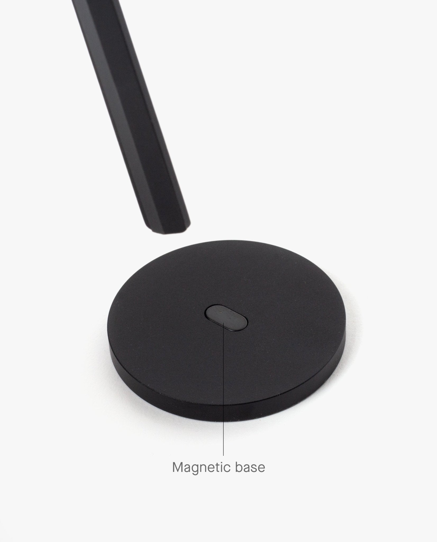 A round, black magnetic metal base is displayed on a white background, with HMM Scissors (Black) hovering above it. A label points to the base, reading "Magnetic base.