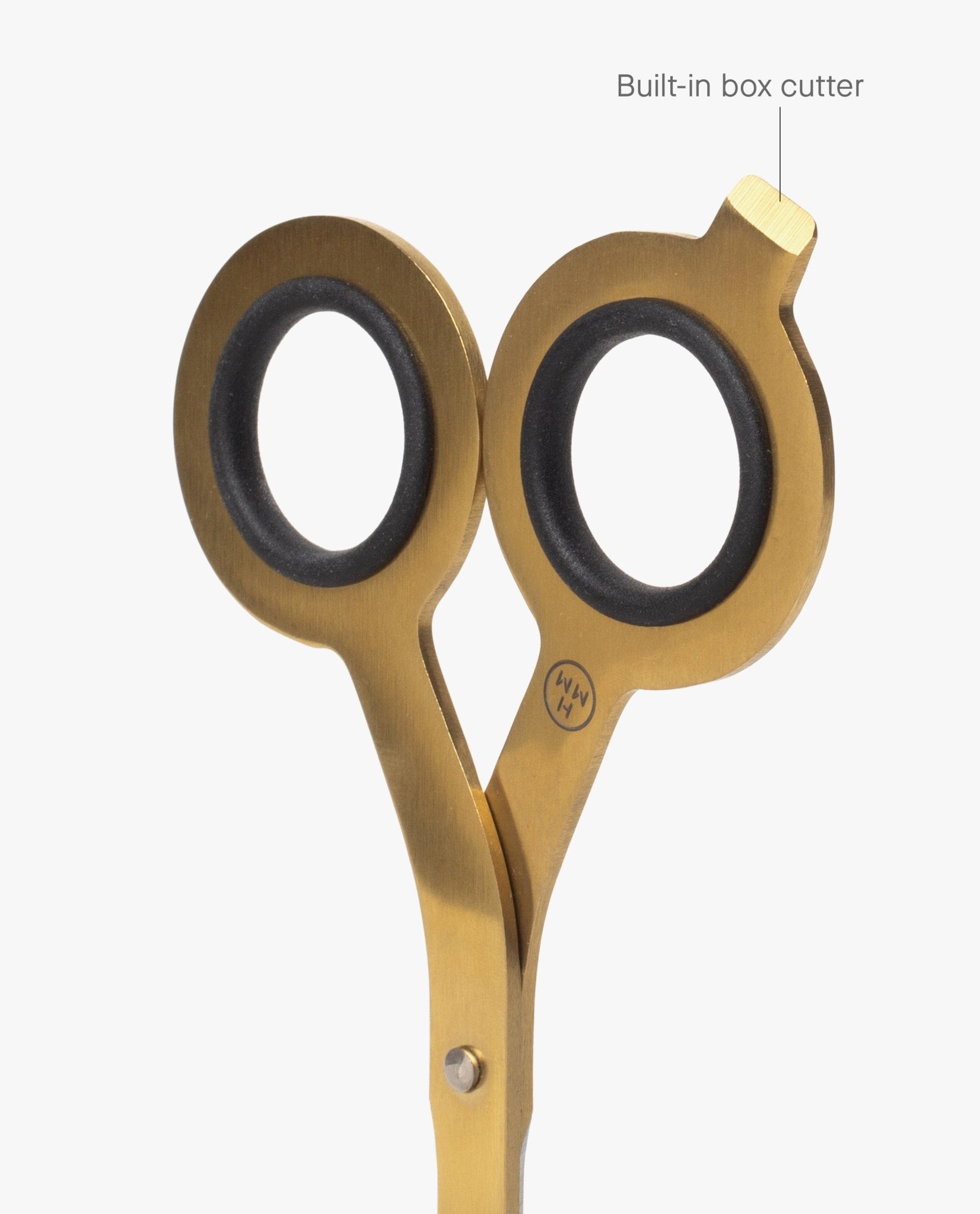 The HMM Scissors (Gold) are crafted from gold stainless steel and feature black finger grips, shown partially open. One handle displays a built-in box cutter at the top right, clearly labeled as such. The scissors are photographed against a clean white background.
