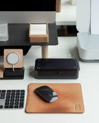 A neatly organized desk with a wireless mouse on a leather mouse pad, keyboard, monitor, note cards in a wooden holder, wireless charging pad, and the sleek Toyo Steel Stackable Storage Box T-190 (Black)—Made in Japan—beside a black box and part of a printer.