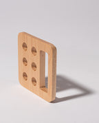 A square maple Gather Pencil Cup Lid, handcrafted in Pennsylvania from solid wood, features five round holes on one side and a large rectangular cutout, casting a shadow on a light surface.