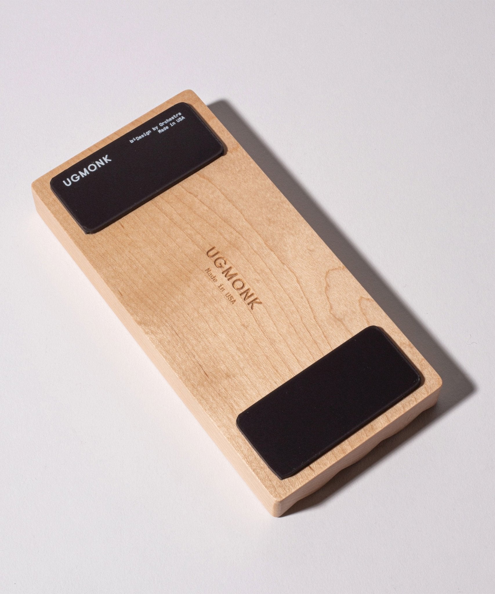 Introducing the Gather Wood Zigzag Tray (2x1 - Maple): this rectangular block is expertly handcrafted from solid maple wood and comes equipped with two black rubber pads on the bottom for stability. The center of the tray is engraved with "UGMONK Made in USA," while the upper left pad features an engraving of "UGMONK" along with product specifications. This elegant piece serves perfectly as a stylish pen tray for your desk or as a sophisticated complement to your existing Wood Zigzag Tray collection.