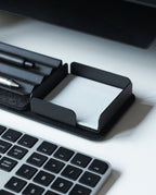 A black keyboard sits next to a sleek black Gather Note Tray (1x1 - Black) containing blank white notepaper, with pens in a tray above it, all on a white desk.