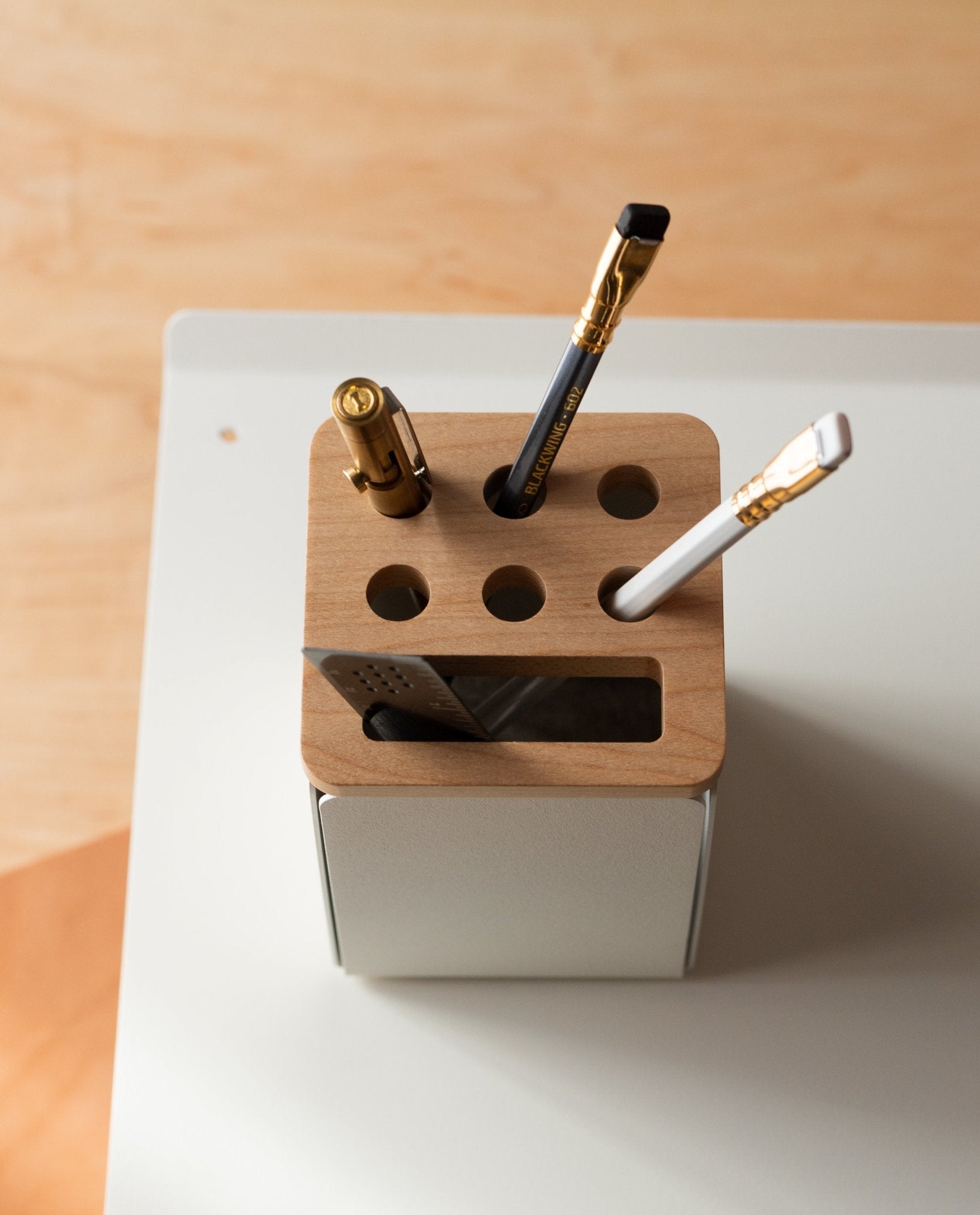 The Warehouse Item - Gather Pencil Cup Lid (Maple), crafted from solid maple wood and made in Pennsylvania, is displayed on a white desk with a light wooden background, elegantly holding three pens and a ruler.