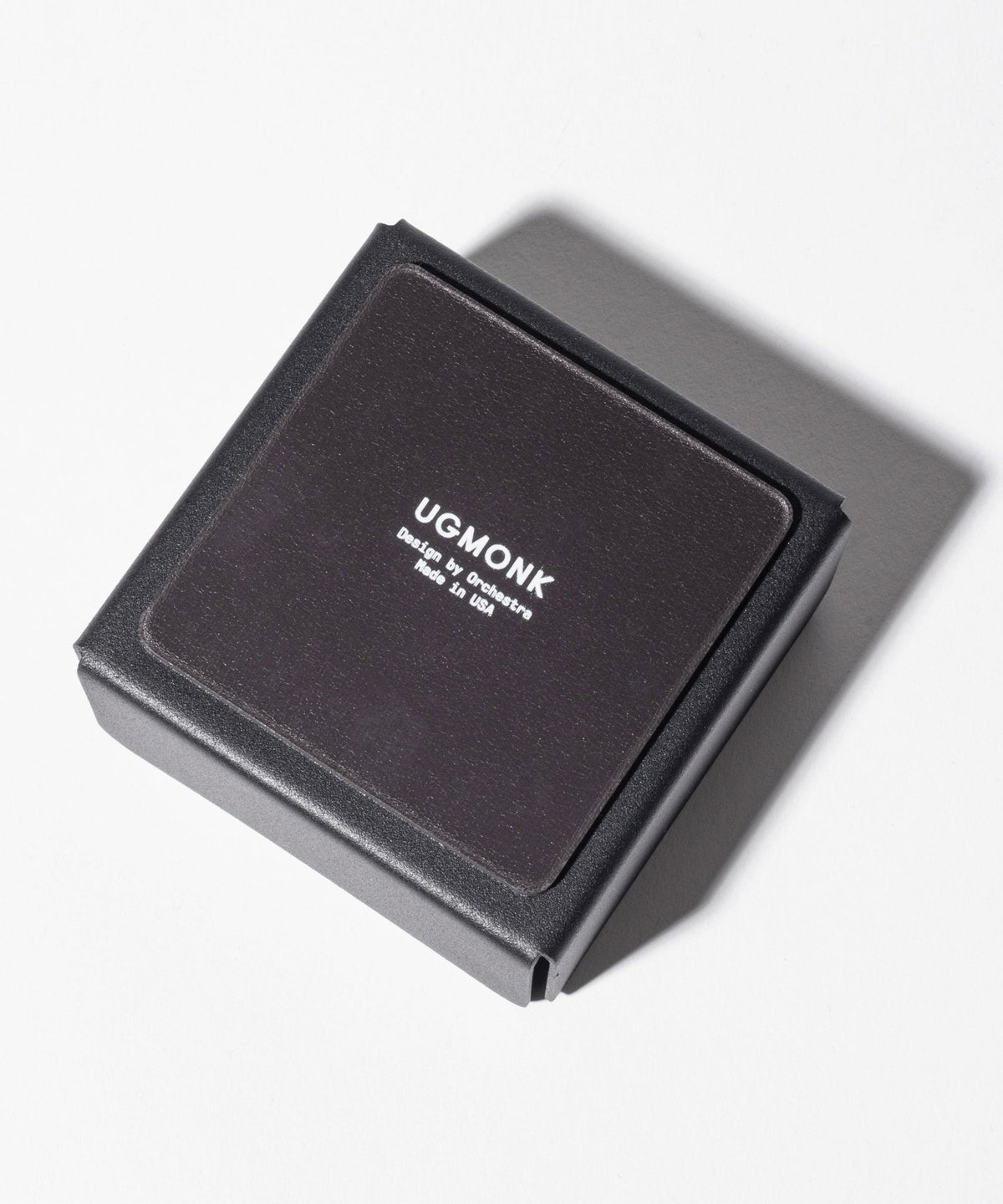 A Gather Small Tray (1x1 - Black), perfect as a desk organizer, featuring "UGMONK" and "Designed by Jeff Sheldon Made in USA" in white text on the lid, rests on a white surface with its shadow to the right. Proudly made in Pennsylvania.