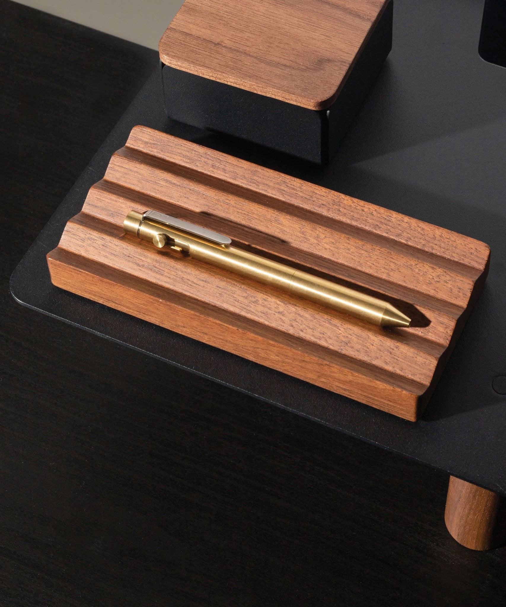 A brass pen sits on the Gather Wood Zigzag Tray (2x1 - Walnut), set on a black surface, with part of a matching pen and pencil holder in the background.