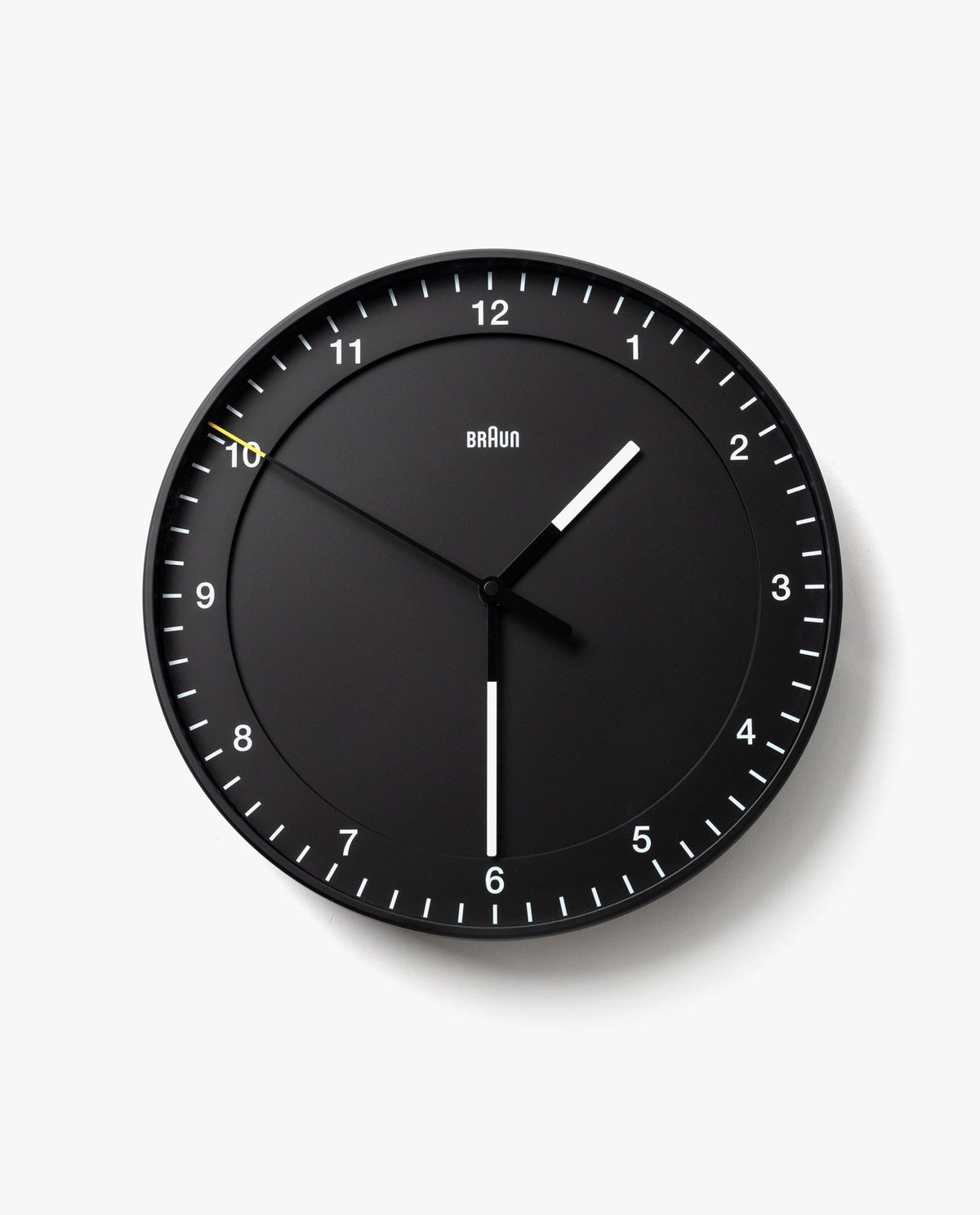 The Braun Wall Clock (Black) features white hour and minute hands, a slim yellow second hand, and silent operation. Clear white tick marks and numbers on a plain white background make the clock easy to read, displaying 10:30:50.