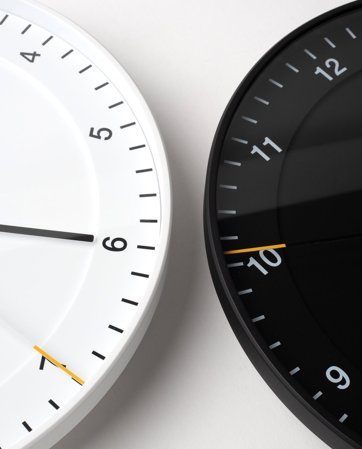 Two Braun Wall Clocks, one in white and one in black, are shown side by side, each featuring an easy-to-read dial and modern design. Both display the time as 6:50. The clocks are cropped to reveal only portions of their faces against a pale background, drawing attention to the Braun Wall Clock (White) and its silent sweeping second hand.