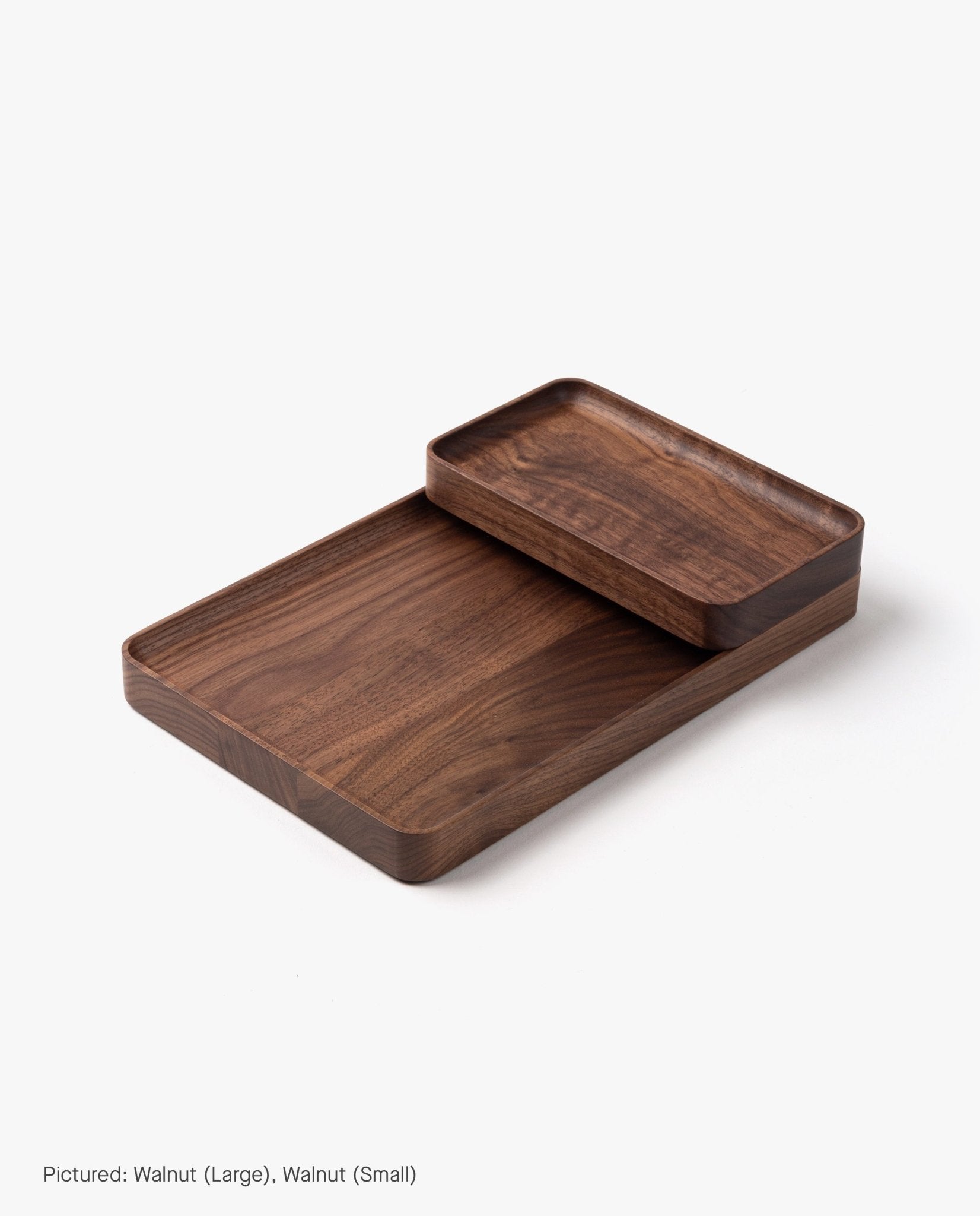 The Small Walnut Valet Tray, handcrafted in Pennsylvania, features rounded edges for elegant everyday carry storage, shown stacked partially atop a larger tray on a white background.
