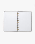 The Discbound Heirloom Journal (Black Leather - Standard 6" x 8.5") features blank white pages and gold rings, lying open on a white background.
