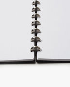 Close-up of the Discbound Heirloom Journal (Black Leather - Standard 6" x 8.5") showing dotted refillable pages and metal disc binding rings, viewed from the bottom center against a white background.