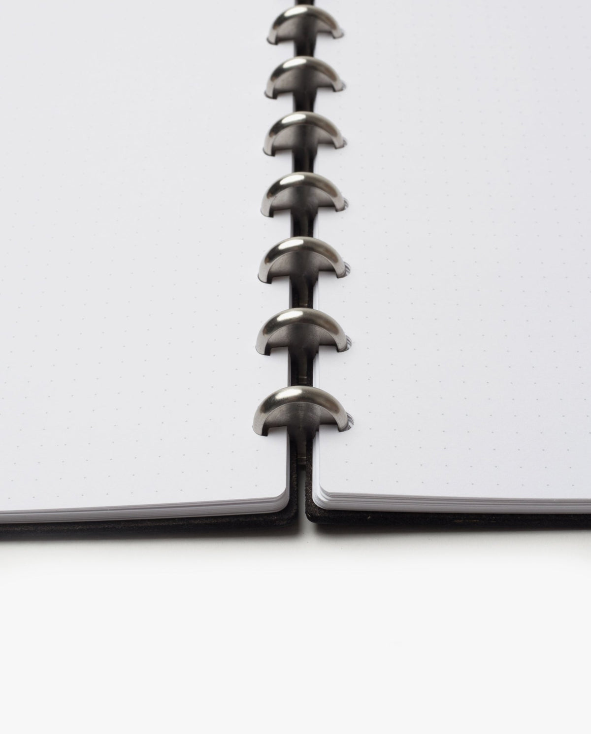 Close-up of the Discbound Heirloom Journal (Black Leather - Standard 6" x 8.5") showing dotted refillable pages and metal disc binding rings, viewed from the bottom center against a white background.