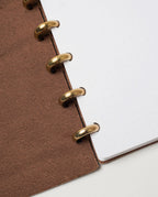 Close-up of an open Discbound Heirloom Journal (Brown Leather - Standard 6" x 8.5") featuring full-grain leather, gold metal rings, and white dot grid paper, displayed on a white surface.