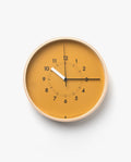 The Lemnos SOSO Clock (Orange) is a minimalist plywood wall clock featuring a mustard yellow face, bold black numbers and hands, a white second hand, and a light wooden frame. This elegant clock displays the time as 10:11:15 and features a silent sweeping second hand for quiet operation against its clean backdrop.