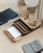 A Valet Tray (Maple - Large) sits on the desk, neatly holding pens, coins, keys, and a notepad. Nearby are a notebook, a grey felt pouch, a lamp, and stacked books for an organized workspace.