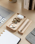 A Valet Tray (Maple – Small), handcrafted from solid maple, holds coins, keys, and wireless earbuds on a light desk. Nearby are a stylus in its holder, an open notebook, a magazine, several books, and part of a laptop sleeve.