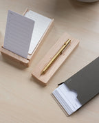 A gold pen rests on the Pen Tray (Maple) beside two wooden notepad stands with lined paper. An open black folder with more notepad sheets is on a light wood desk, showcasing classic organization made in Pennsylvania.